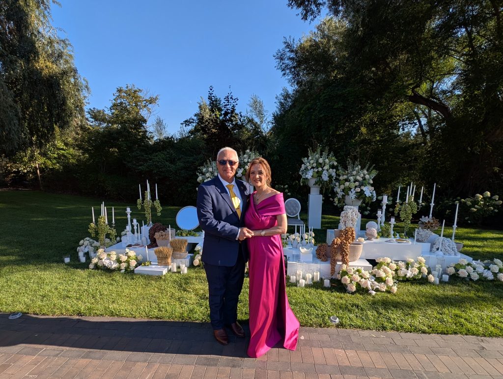 Daryoush Ghashghai, picture with bride's mother Daryoush Ghahghai officiating a bilingual wedding ceremony in Canada, standing with the bride’s mother beside a traditional sofreh aghd setup in an outdoor garden