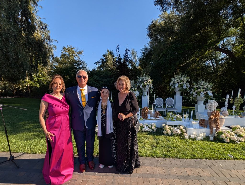 Daryoush Ghashghai, picture with bride's family 2 of 2 Daryoush Ghashghai officiating a bilingual wedding ceremony in Canada, standing with the bride’s family beside a traditional sofreh aghd setup in an outdoor garden (image 2 of 2)